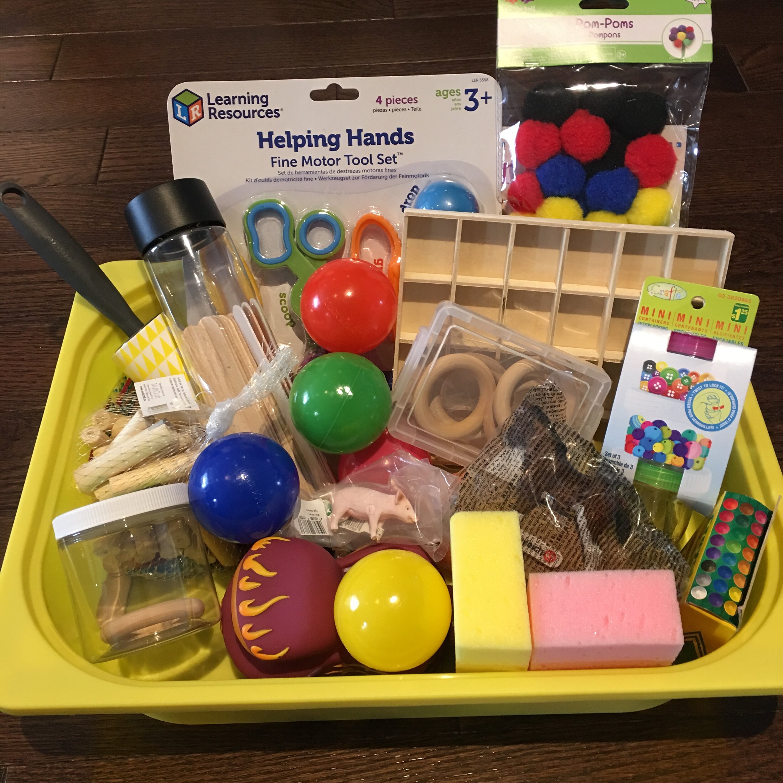 An example of a gift for a 1-3 year old. An IKEA TROFAST bin filled with items that can put inside to play with including lose parts, animal figurines, jars, pompoms, cars, sponges, a try and some motor tools from Learning Resources.