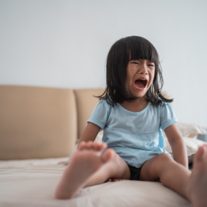 a crying toddler sitting on a bed