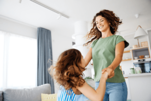 A mother holding hands and laughing with her young daughter at home