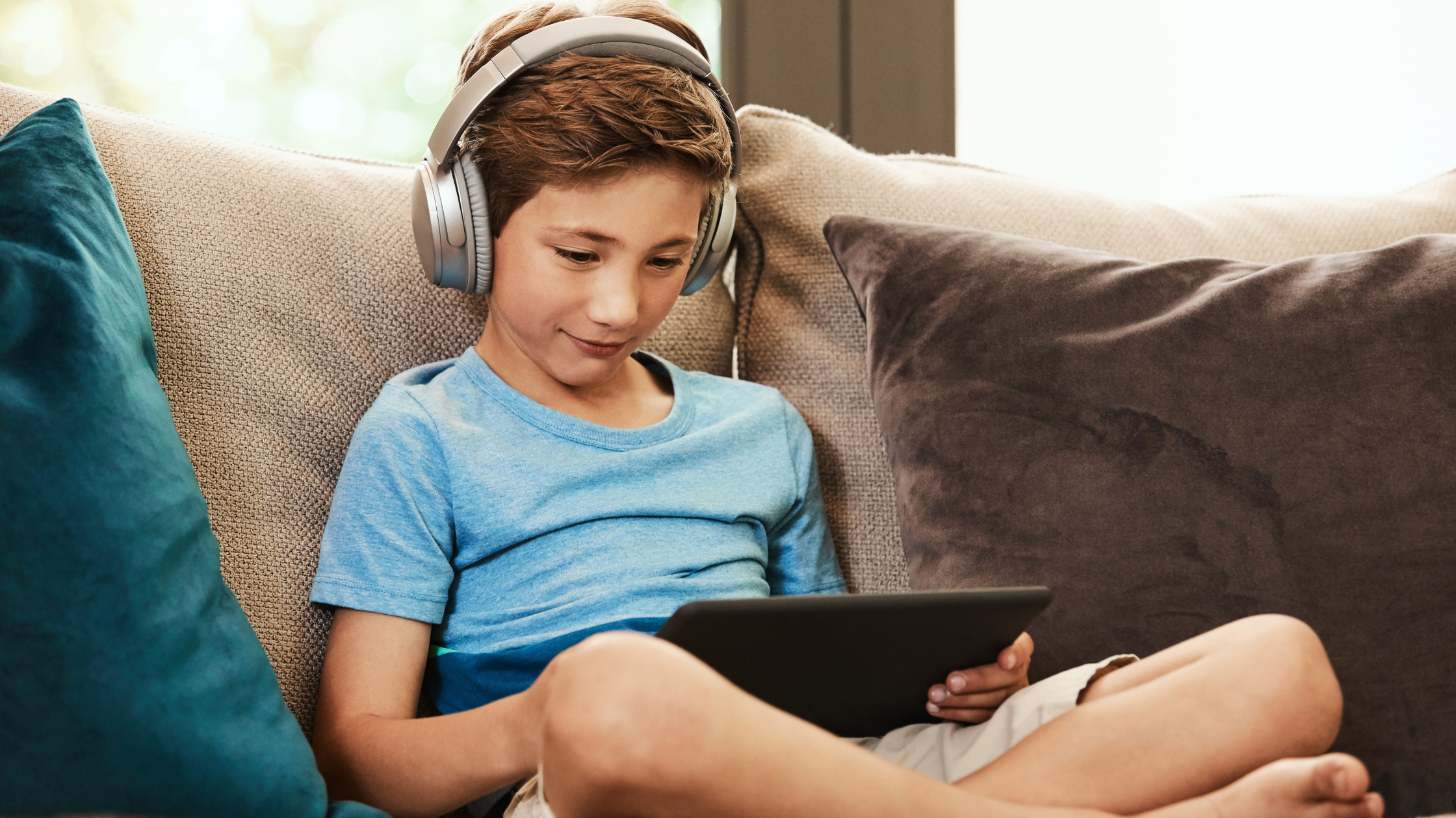 child sitting on couch with headphones and an ipad using social media