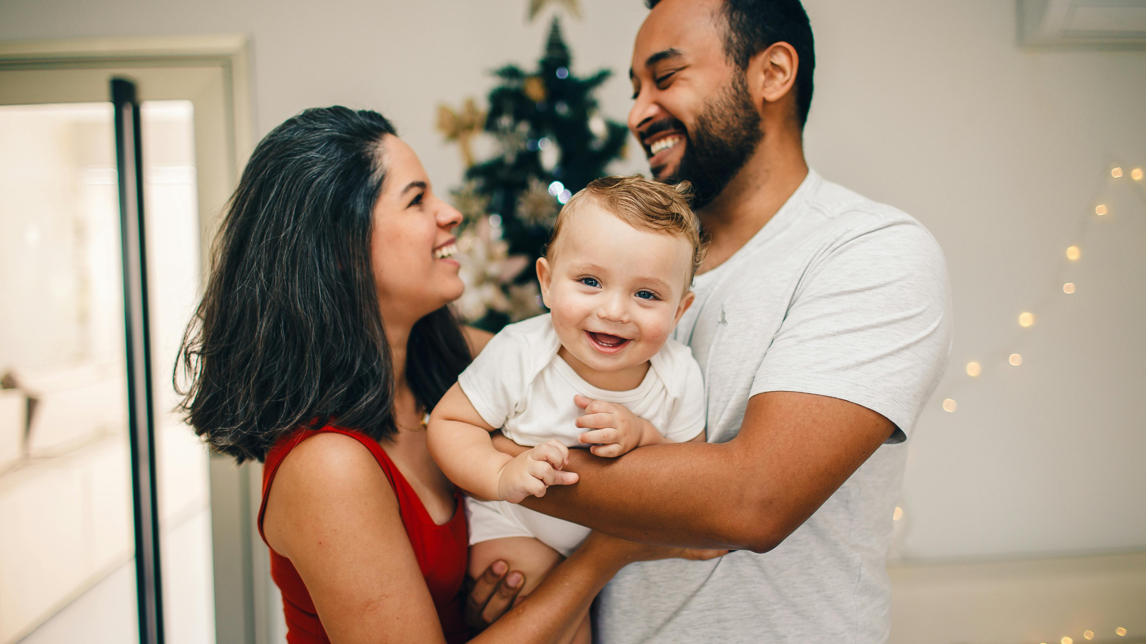 mother and father look at each other lovingly while their baby smiles in their arms